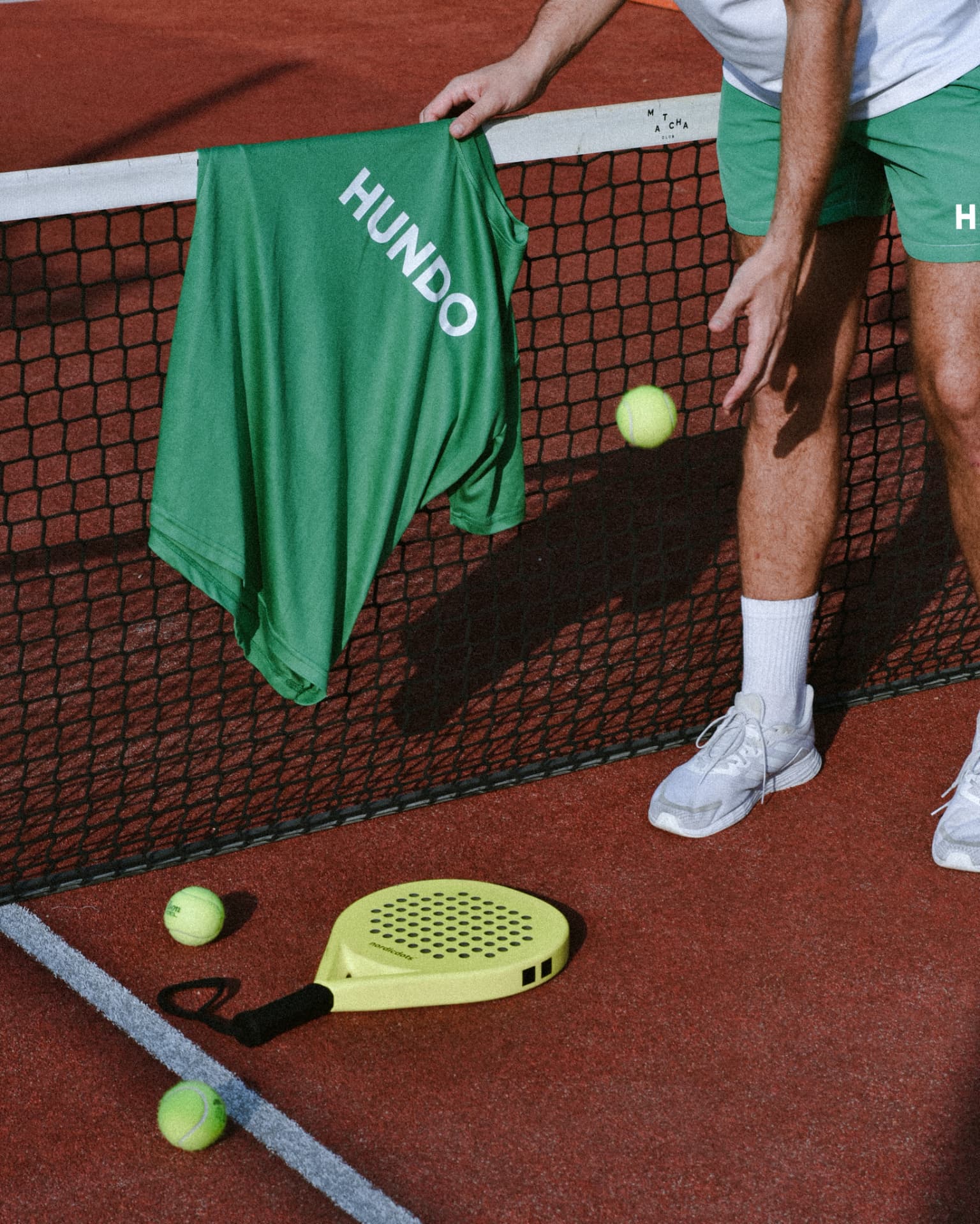 HUNDO green jersey hanging over a padel net